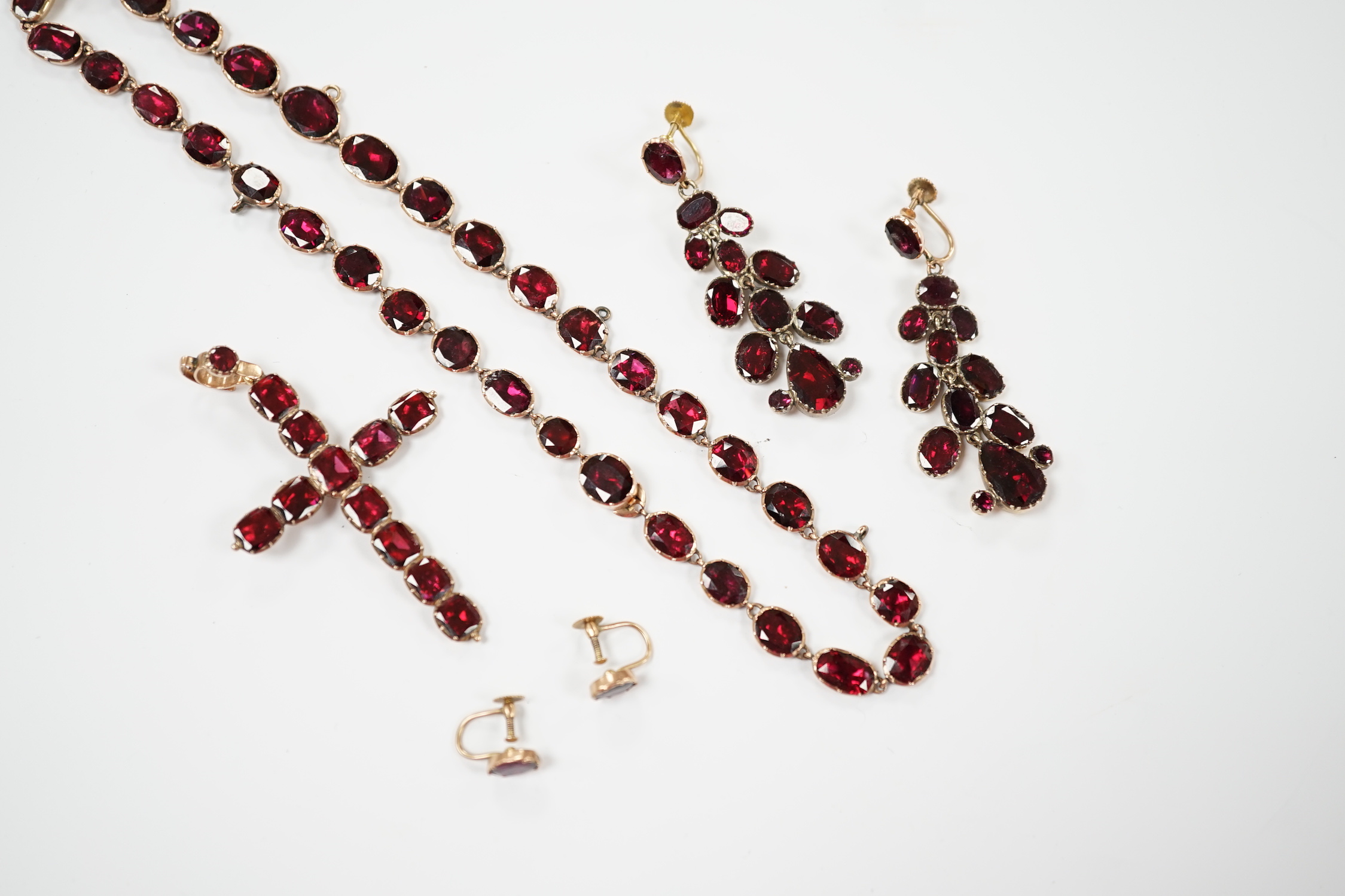 Six items of Victorian oval cut garnet set jewellery, including a yellow metal necklace (lacking drops?), 37cm, a pair of 9ct ear clips, a yellow metal cross pendant with cushion cut stones, gross weight 30 grams and a p